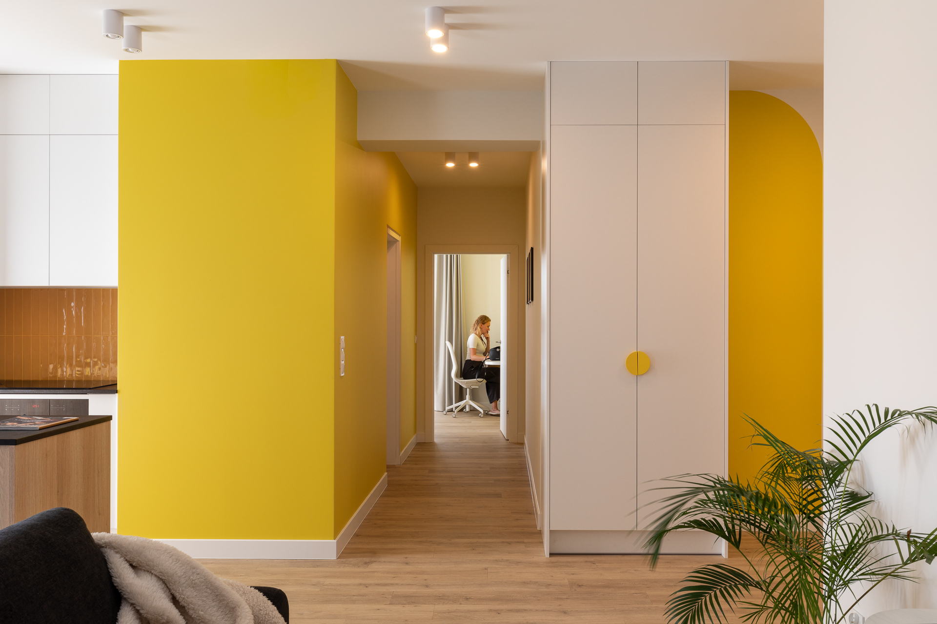 Żółty hol nowoczesnego apartamentu w Katowicach z szafą, rośliną i widokiem na kuchnię oraz pokój