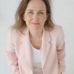 Kobieta w jasnoróżowej marynarce na jasnym tle, portret do materiałów o apartamentach na wynajem